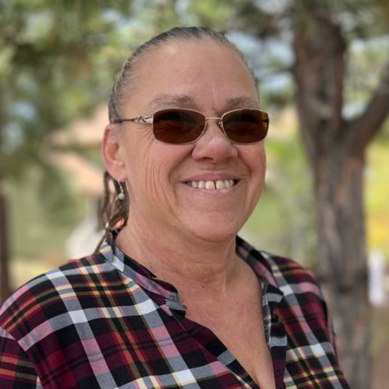 An image of a woman with tinted glasses and brown hair smiling.